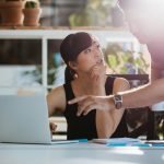 Woman sitting at her desk with man pointing at laptop